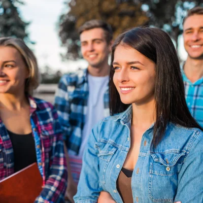 grupa studentów stojących na zewnątrz kampusu uczelni, w casualowych ubraniach, patrzących w dal